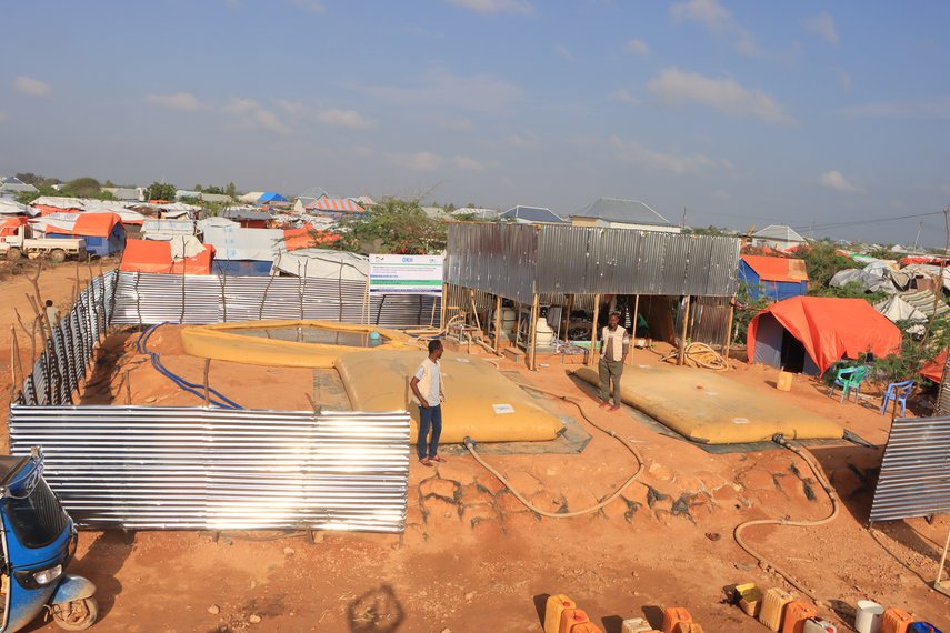 Trinkwasseraufbereitungsanlage in Somalia, umgeben von Zelten, zwei Personen stehen daneben.