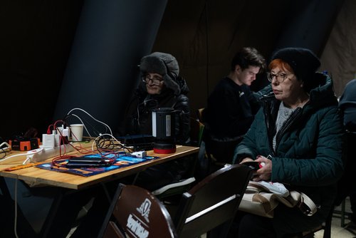 Bewohner erhalten in einem Zelt an einer von der Regierung betriebenen humanitären Hilfsstelle heiße Getränke, während andere sich aufwärmen und ihre Geräte während eines Stromausfalls aufladen, nachdem wichtige zivile Infrastruktur durch russische Raketen- und Drohnenangriffe getroffen wurde, inmitten des russischen Angriffs auf die Ukraine, in Kyjiv, Ukraine, Januar 2026.