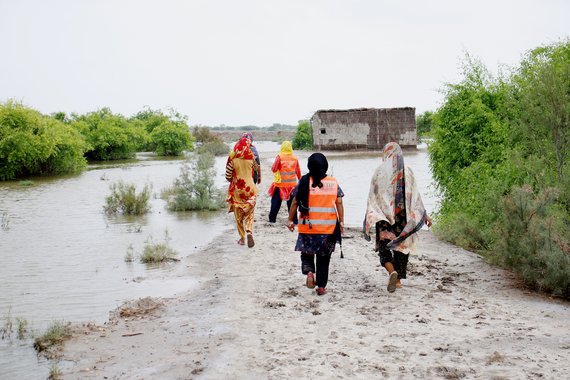 Helfende und Betroffene gehen durch ein überschwemmtes Dorf
