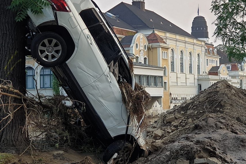 Ein demoliertes Auto steht hochkant an einem Baum, umgeben von Schlamm und Geröll. 