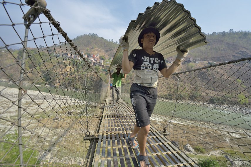 In Nepal wird Wellblech für Dächer über eine Hängebrücke getragen.