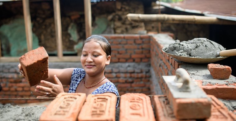 Eine Frau in Nepal platziert einen Ziegelstein.