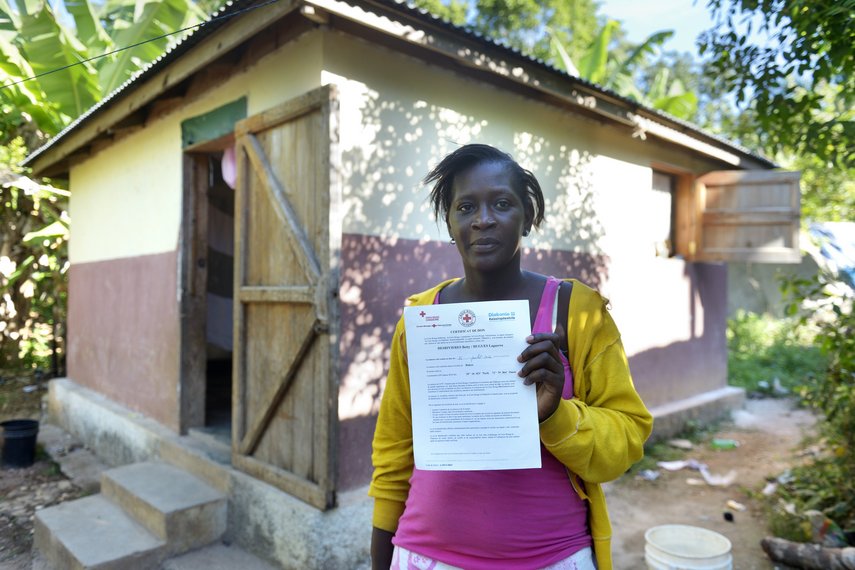Frau mit neu gebautem Haus auf Haiti